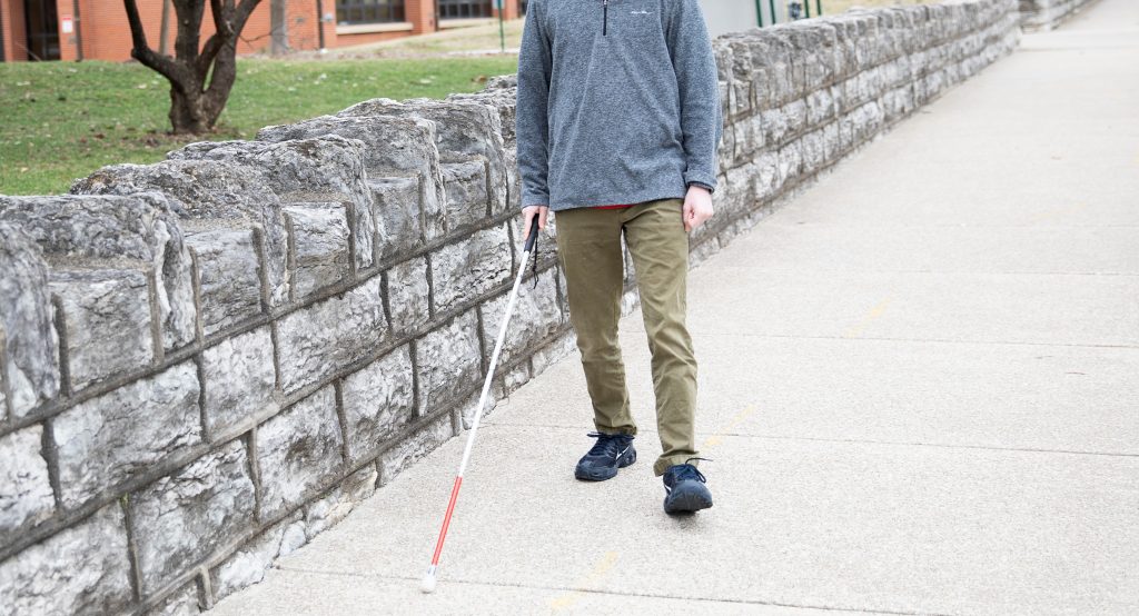 A young male walking down the street holding a white cane.