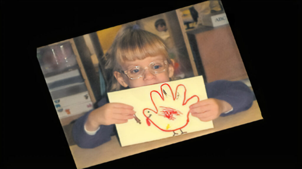 A child holding up one of her creative art activities of a tactile turkey hand print craft.