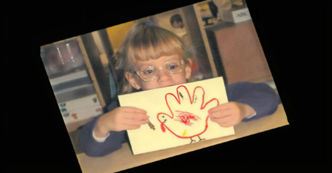A child holding up one of her creative art activities of a tactile turkey hand print craft.