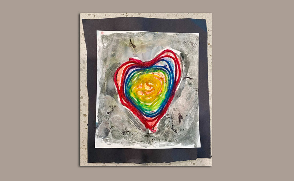 Black cardstock with a rainbow-colored yarn in the shape of a filled heart.