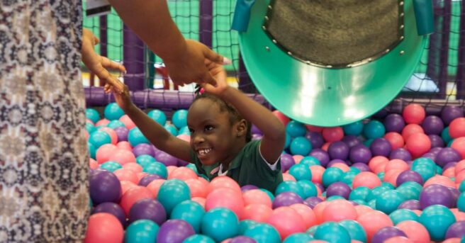 young girl playing in a ball pit reaching to an adult