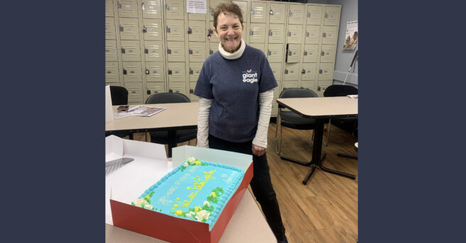 Amy Bovaird standing beside a large sheet cake she made