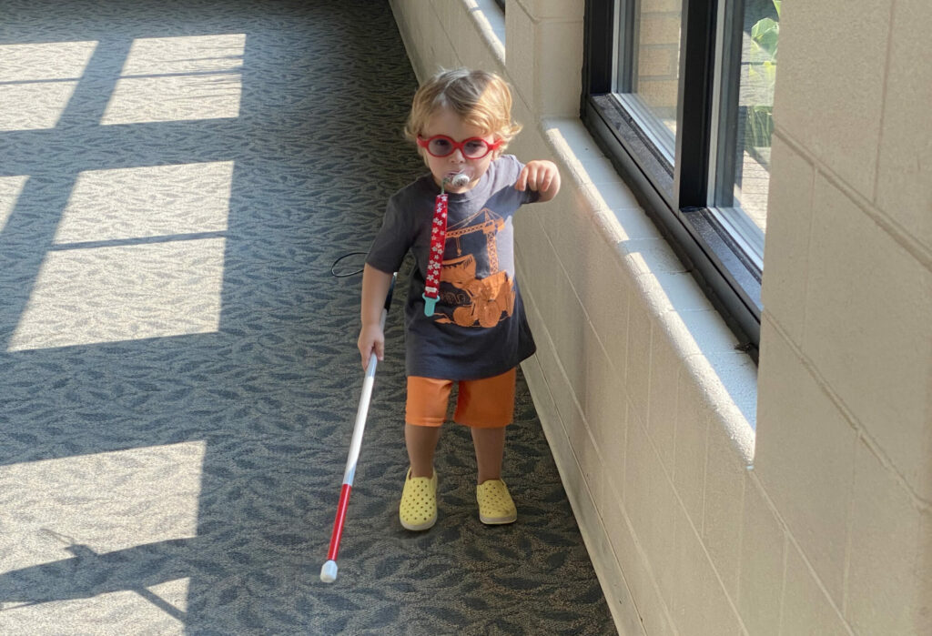 A young child walking in a hallway with a cane.
