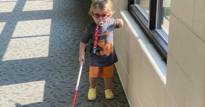 A young child walking in a hallway with a cane.