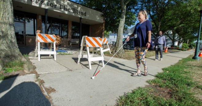 person using white cane to walk down sidewalk --photo provided by Guide Dogs for the Blind