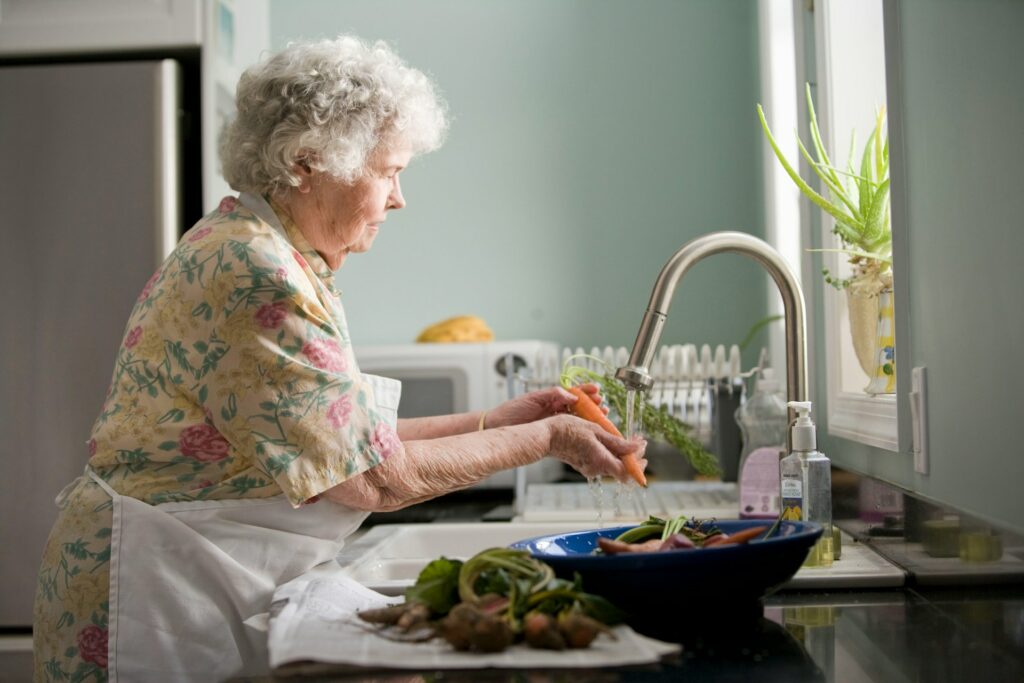 older woman washing vegetables in a home kitchen