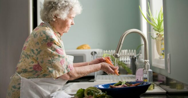 older woman washing vegetables in a home kitchen