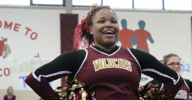 Cheerleader mid-cheer wearing “Wildcats” uniform.