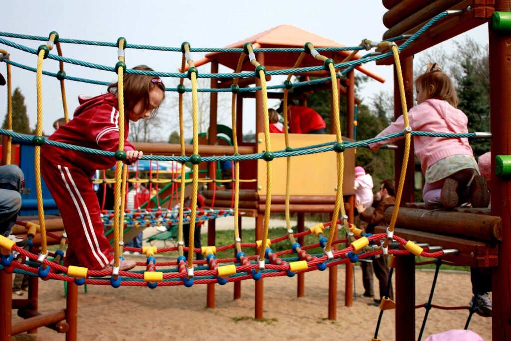 Children playing on a rope bridge and a fort outside at a playground.