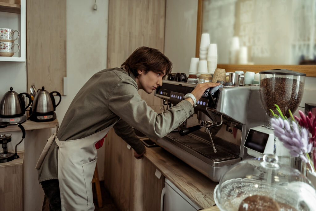 Teen wearing an apron working in a restaurant adjusting a coffee machine.