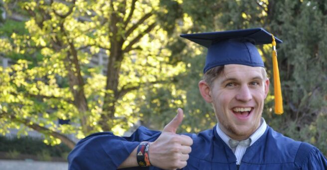 College graduate in cap and gown giving a "thumbs up"