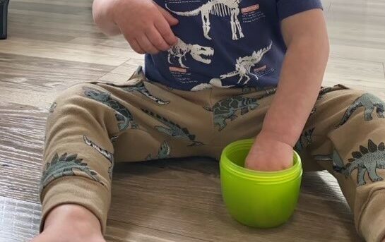 A toddler sitting with their hand in a snack cup.
