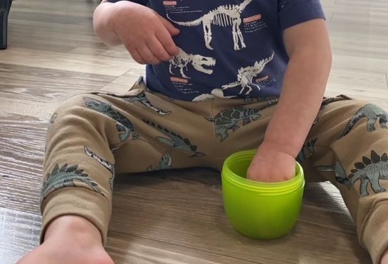 A toddler sitting with their hand in a snack cup.