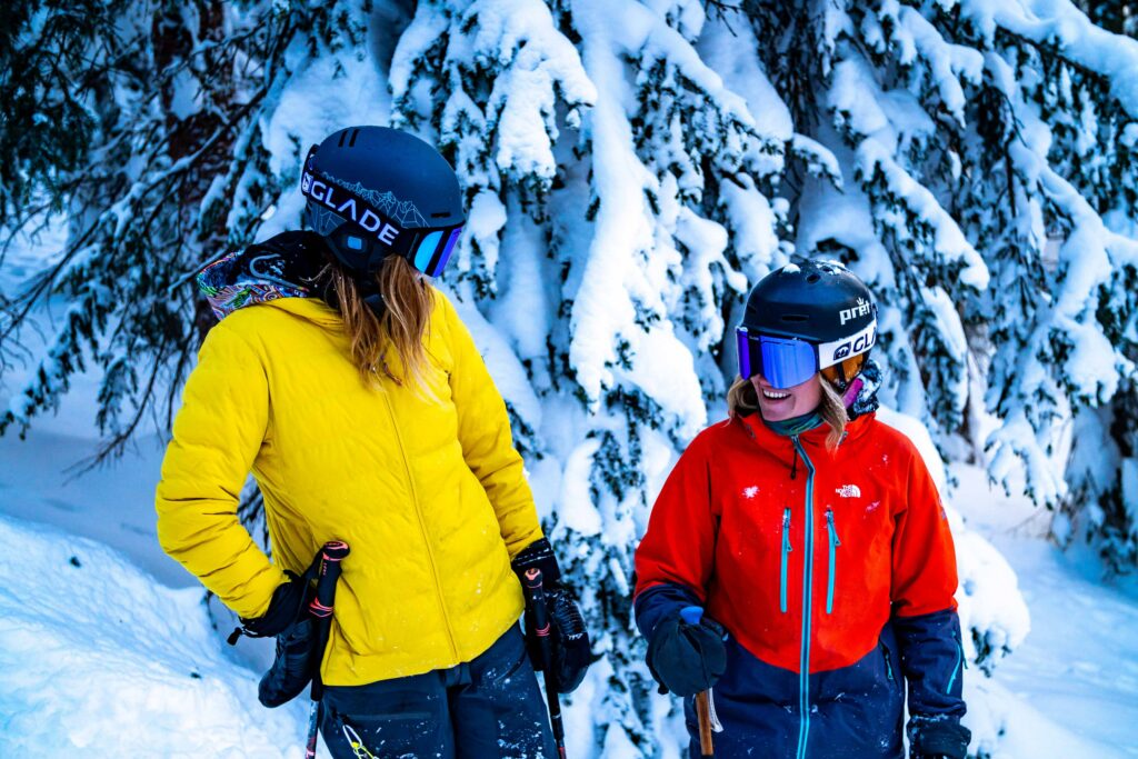 Two people in brightly colored ski gear in a snowy background