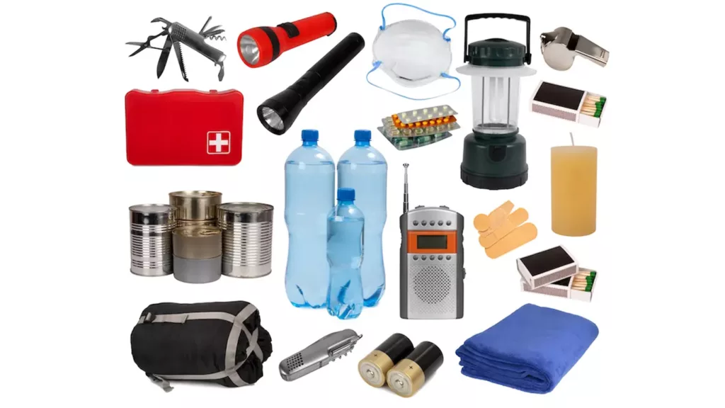 A collection of emergency preparedness supplies including bottled water, canned food, flashlights, a lantern, a first aid kit, a radio, batteries, a sleeping bag, a blanket, candles, matches, a multi-tool, face masks, bandages, and a whistle.