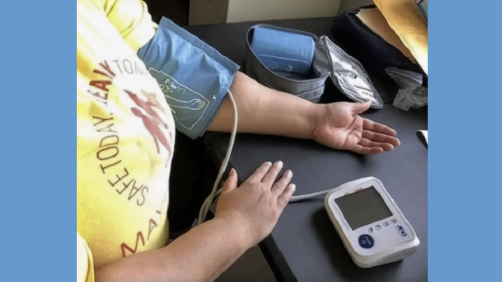 woman taking blood pressure. She has the cuff on her arm and the monitor on the table in front of her.