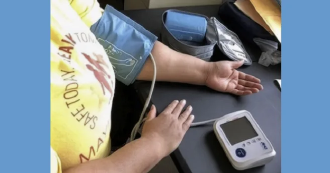 woman taking blood pressure. She has the cuff on her arm and the monitor on the table in front of her.