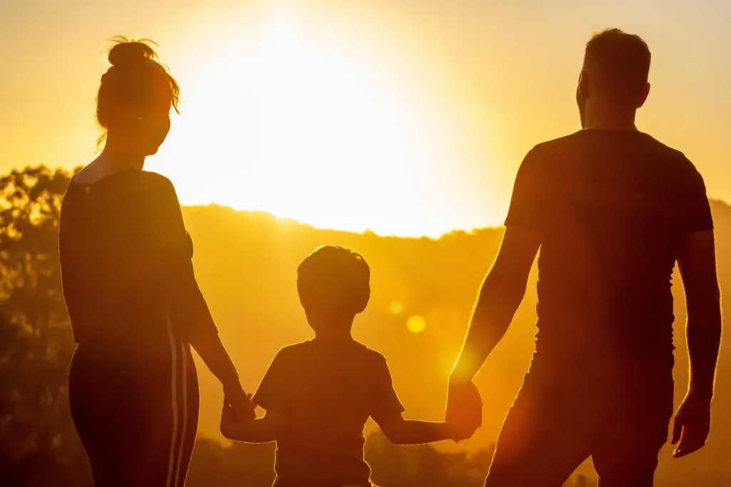 Two adults and a child holding hands at sunset.
