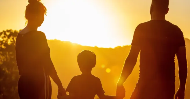 Two adults and a child holding hands at sunset.