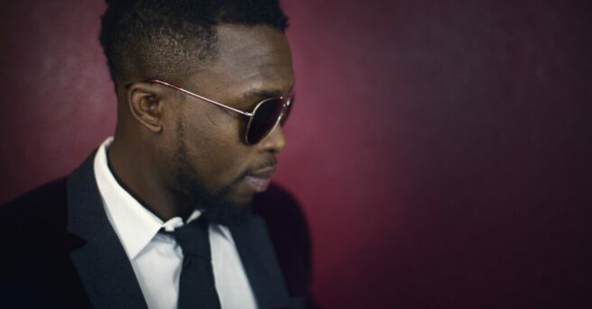 Black man wearing sharp black suit and aviator sunglasses.