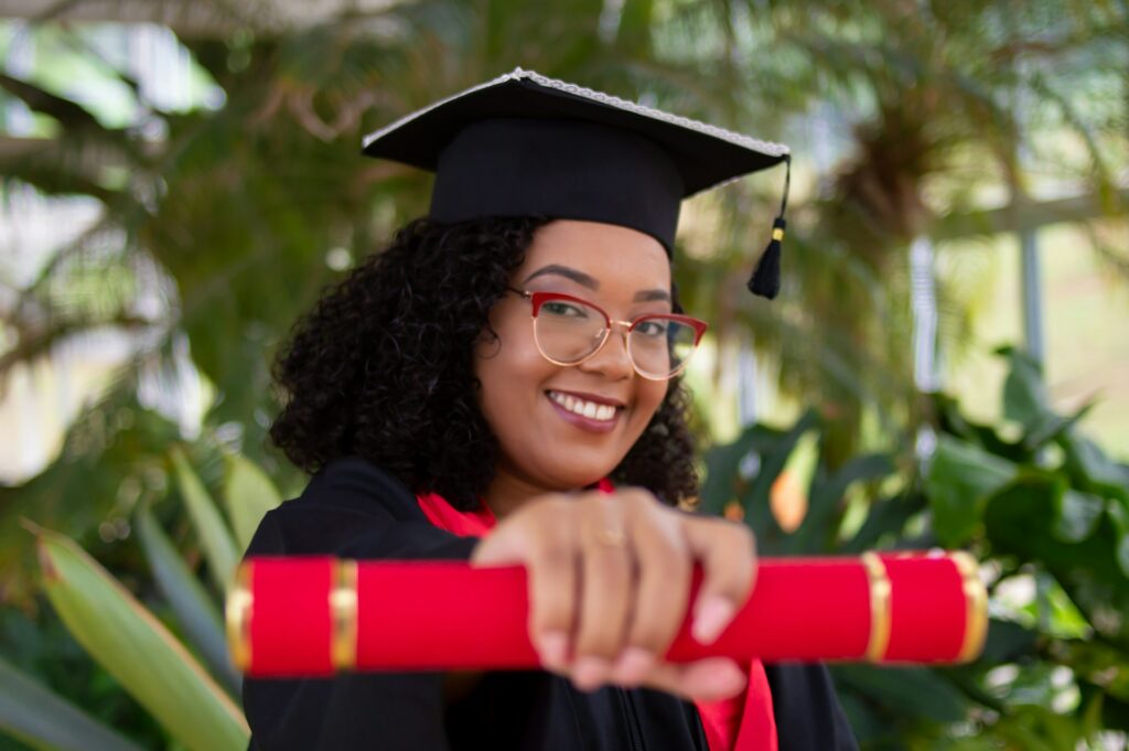 young person with curly hair and eyeglasses wears a graduation cap and gown