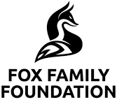 Fox family foundation log black and white fox sitting with tail wrapped around its feet looking over right shoulder.