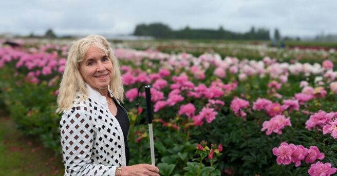 Gena Harper holding a white cane in front of a field of flowers