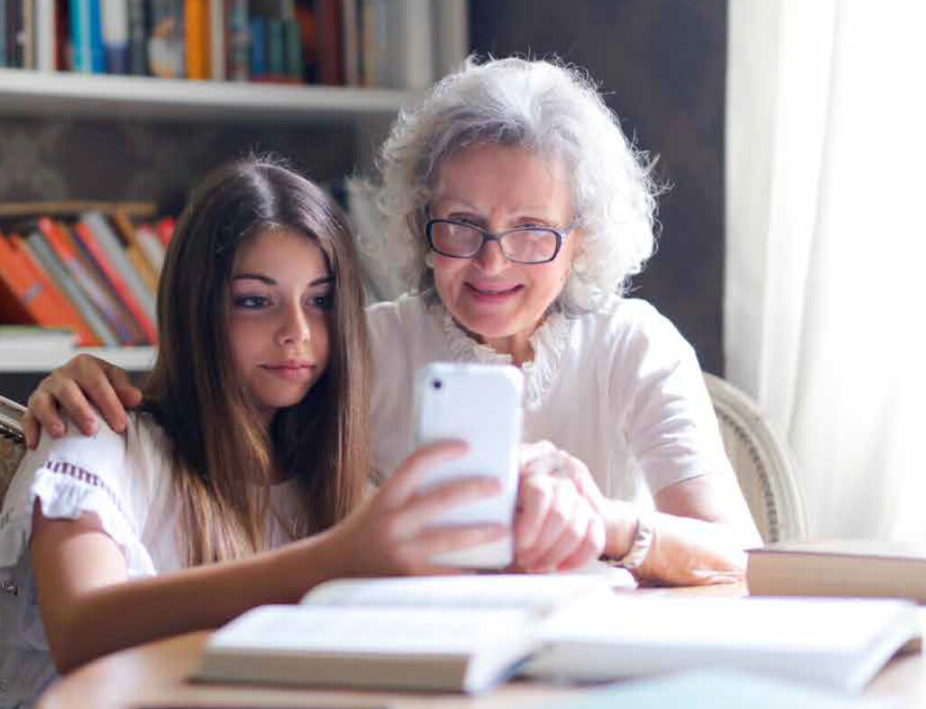 Una abuela sentada con su nieta viendo un teléfono.