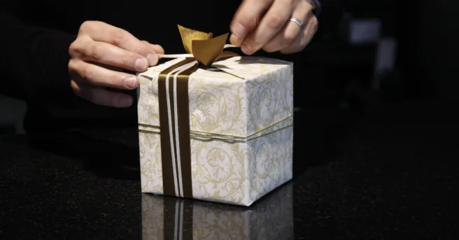 hands tie a bow on a small gift