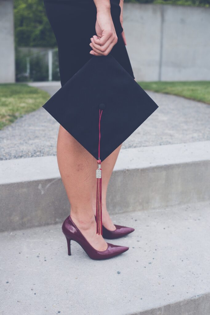 Photo of a woman standing while holding a graduation cap at her knees