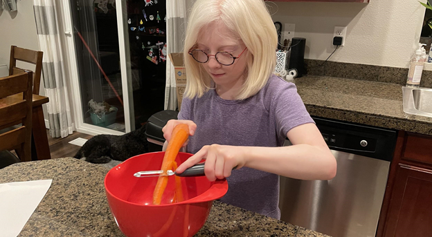 Young girl with glasses peeling a carrot into a bowl.