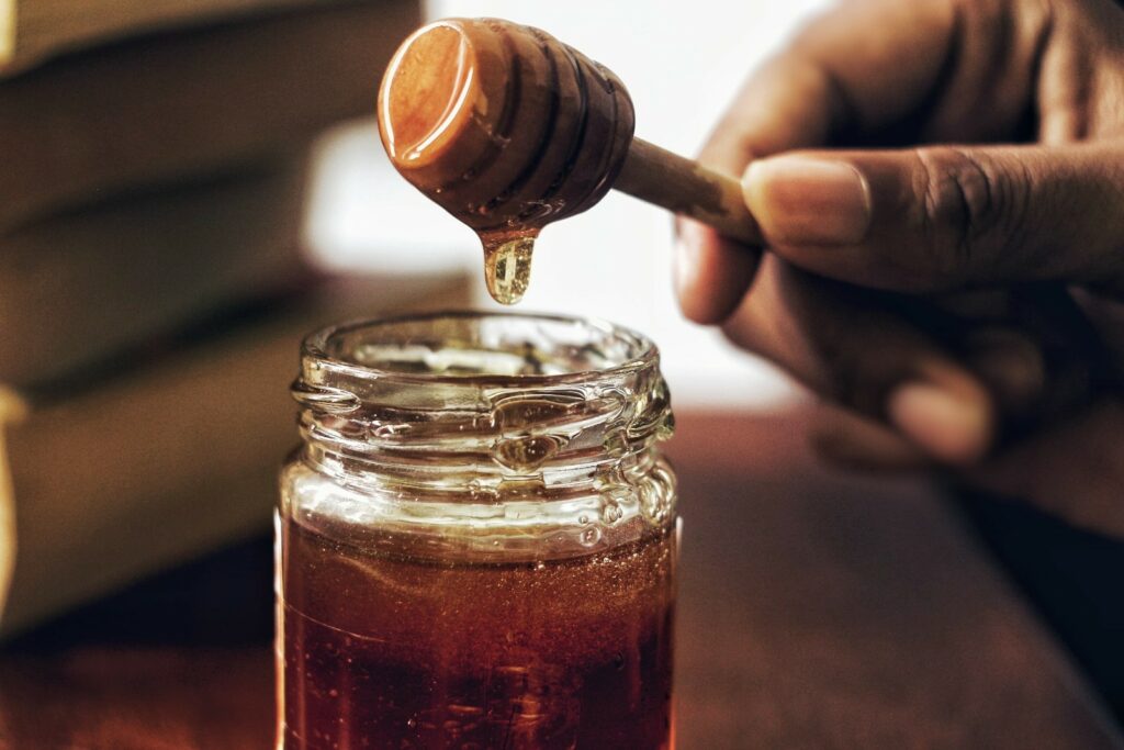 jar of honey and drop of honey dripping from honey dipper