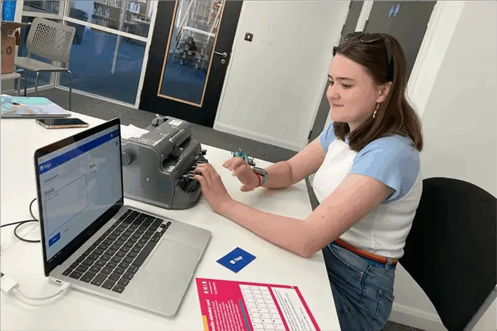 An adult sitting at a table with a traditional braille writer using Paige Connect and the Paige Braille website. 