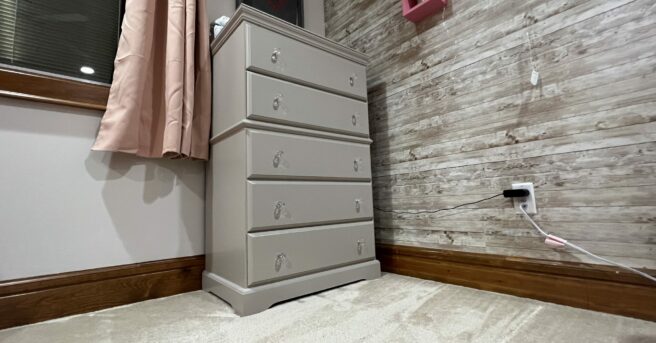A tan dresser in the corner of a bedroom.