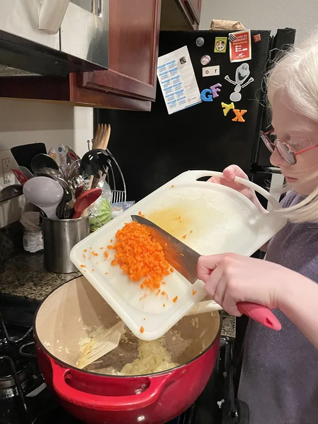 Young girl with glass scrapping vegetables off a chopping board with a knife