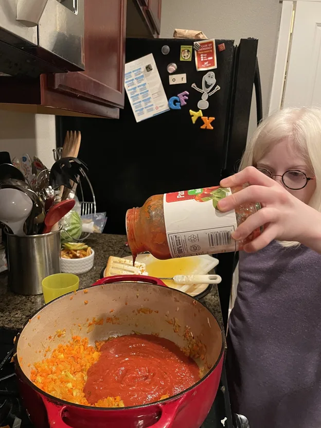 Young girl with glasses pouring pasta sauce