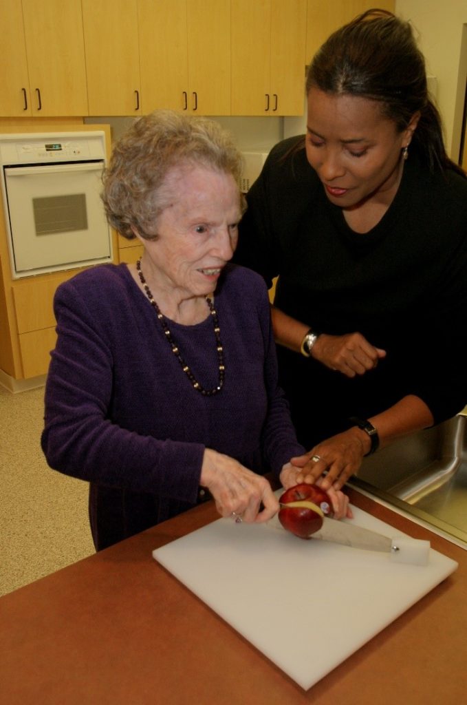 VRT showing older woman how to slice an apple using a knife attached to a white cutting board
