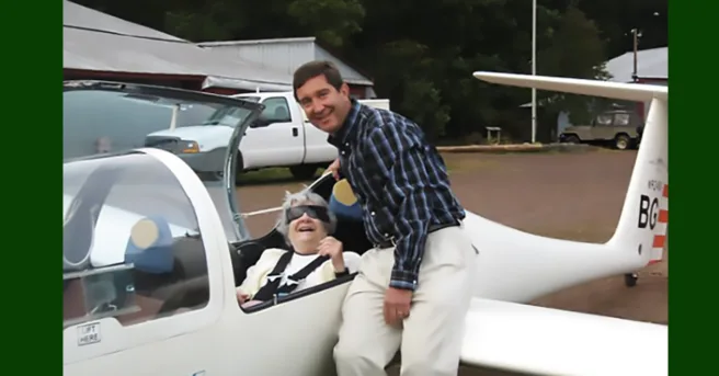 Jane Henkler is smiling and sitting inside a plane while her son, Ed, is also smiling and leaning on the wing.