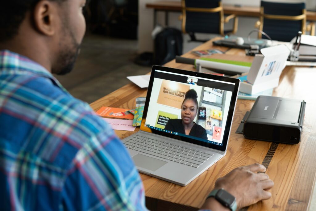 Man sitting at a table talks to a woman in a zoom meeting on a laptop.