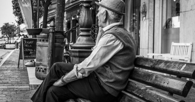 Senior sitting alone on a park bench of a city street.