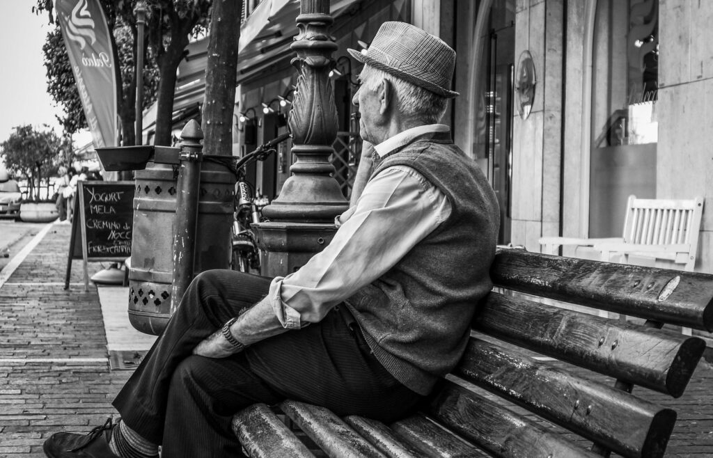 Senior sitting alone on a park bench of a city street.