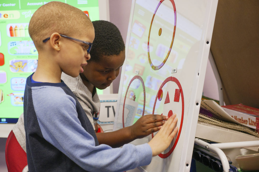 Two young boys playing with red magnets on a white board