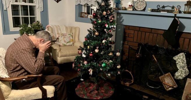 man with head in hands sitting by Christmas tree alone depicting depression during the holidays.