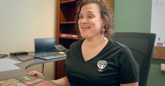 Tai Tomasi sitting at a desk wearing an APH shirt