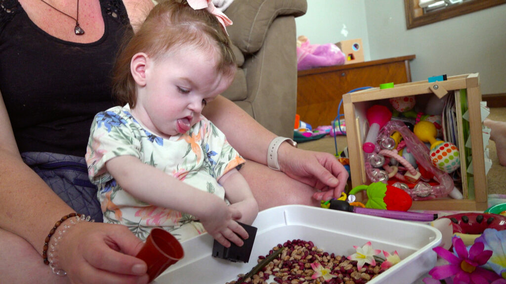 A young child playing in a sensory bin with various toys behind her