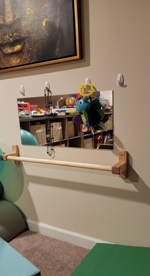 In the picture, there is a pull-up bar. Over the pull-up bar, there is a mirror glued to the wall. And over the mirror, there are four hooks with some toys.