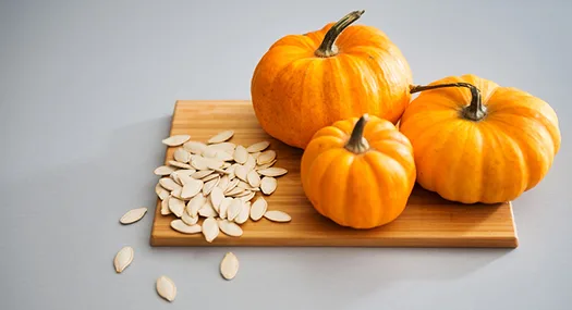 three mini pumpkins and seeds on a cutting board