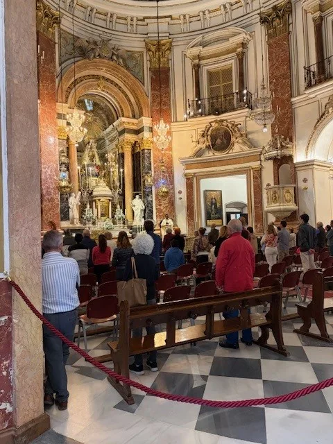 People stand during a service inside an ornate church with gilded arches and marble columns.”