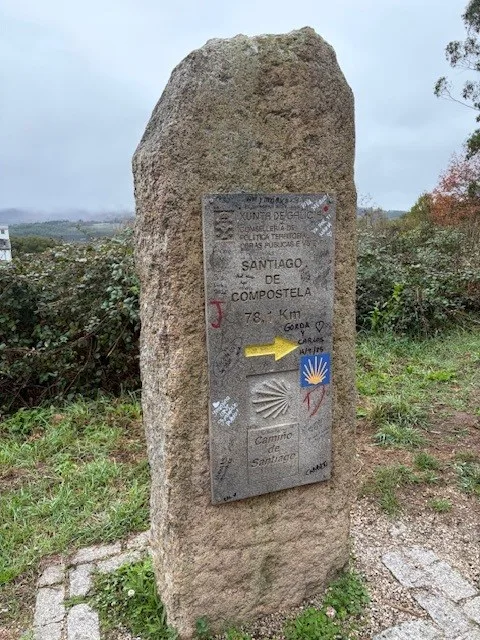 Stone Camino de Santiago marker pointing toward Santiago de Compostela with the yellow arrow and scallop shell.