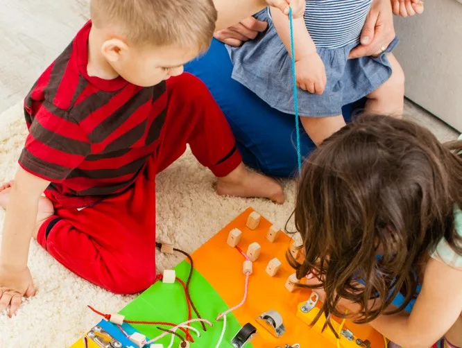 Three toddlers playing with a busy board. 